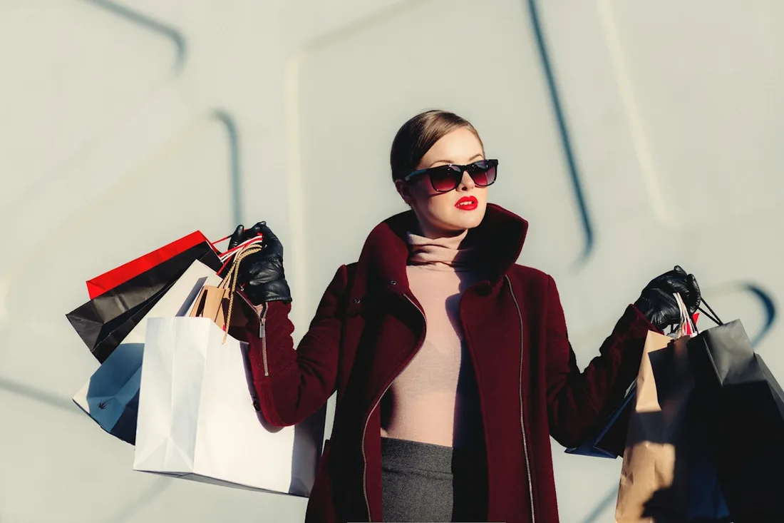 Woman wearing a dark coat and sunglasses while carrying shopping bags