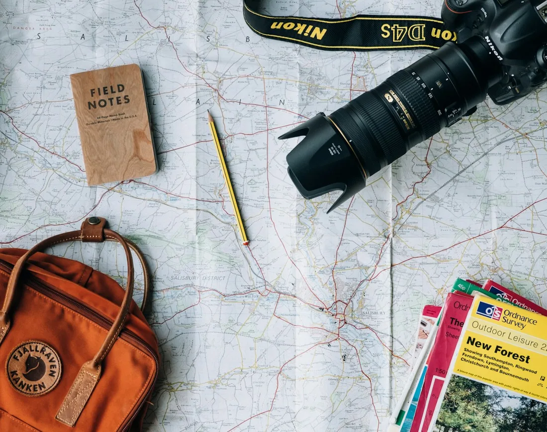A map, camera, notebook, and leather travel bag arranged on a table
